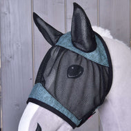 Nahaufnahme eines Pferdes mit der Fliegenmaske de Luxe Turquoise von Hobby Horse LarDen, einer waschbaren Fliegenmaske aus schwarzem Netzmaterial mit türkisfarbener Einfassung, die zum Schutz Augen und Ohren bedeckt. Holzverkleidung im Hintergrund.