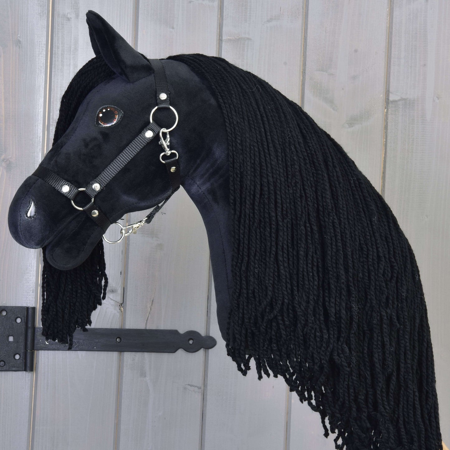 Hobby Horse Maximus avec licol noir de Hobby Horse LarDen, avec design d’étalon noir fait main, épaisse crinière noire en fil et bride, présenté sur fond en bois clair.