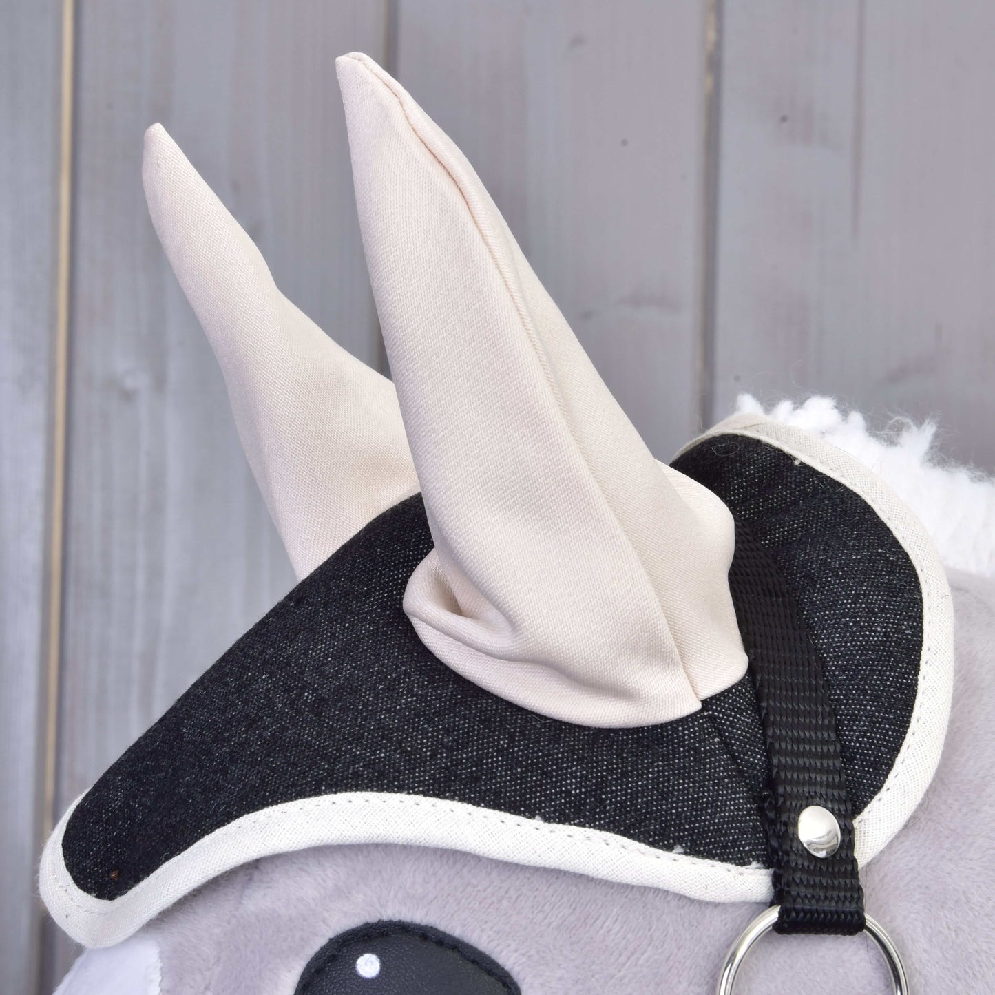 Nahaufnahme des grauen Plüsch-Set Blue Denim Hobby Horse von Hobby Horse LarDen mit schwarz-weißem Stoffzaumzeug und weichen cremefarbenen Ohren – eine charmante Dekoration für jeden Fan.