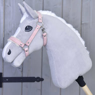 Hobby Horse LarDen Halfter mit Fell - Kunstleder Mullbery an einem hellgrauen Hobby Horse aus Plüsch mit weißer Mähne, rosa Zaumzeug aus Kunstleder und gestickten Details, auf einem Holzstab vor einer grauen Holzwand.