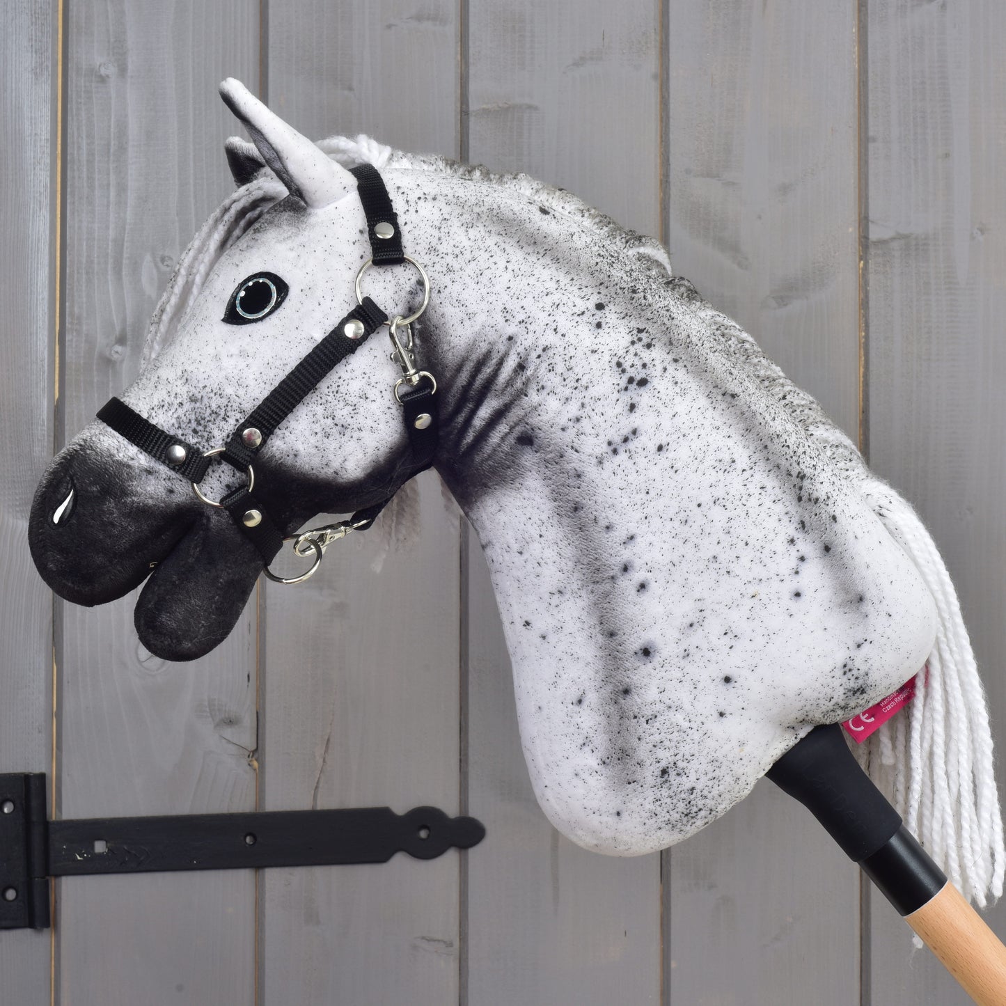 Hobby Horse Naivy avec licol noir - taille S de Hobby Horse LarDen, avec une tête d’étalon réaliste grise et noire et un licol noir, présenté devant un mur en bois gris.