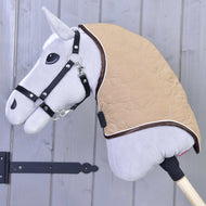 Nahaufnahme von Hobby Horse LarDen Halsteil Bonanza – ein graues Hobby Horse mit schwarzem Zaumzeug und hellbrauner gesteppter Decke mit sicheren Verschlüssen – auf einem Holzstab vor einer grauen Holzwand.