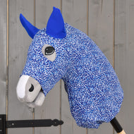 Nahaufnahme von Hobby Horse LarDen „Hobby Horse Schutzanzug See (Lycra)“ mit blau-weißem PES-Stoff, blauen Ohren und grauer Schnauze, auf einem Holzstab vor grauem Holz-Hintergrund.