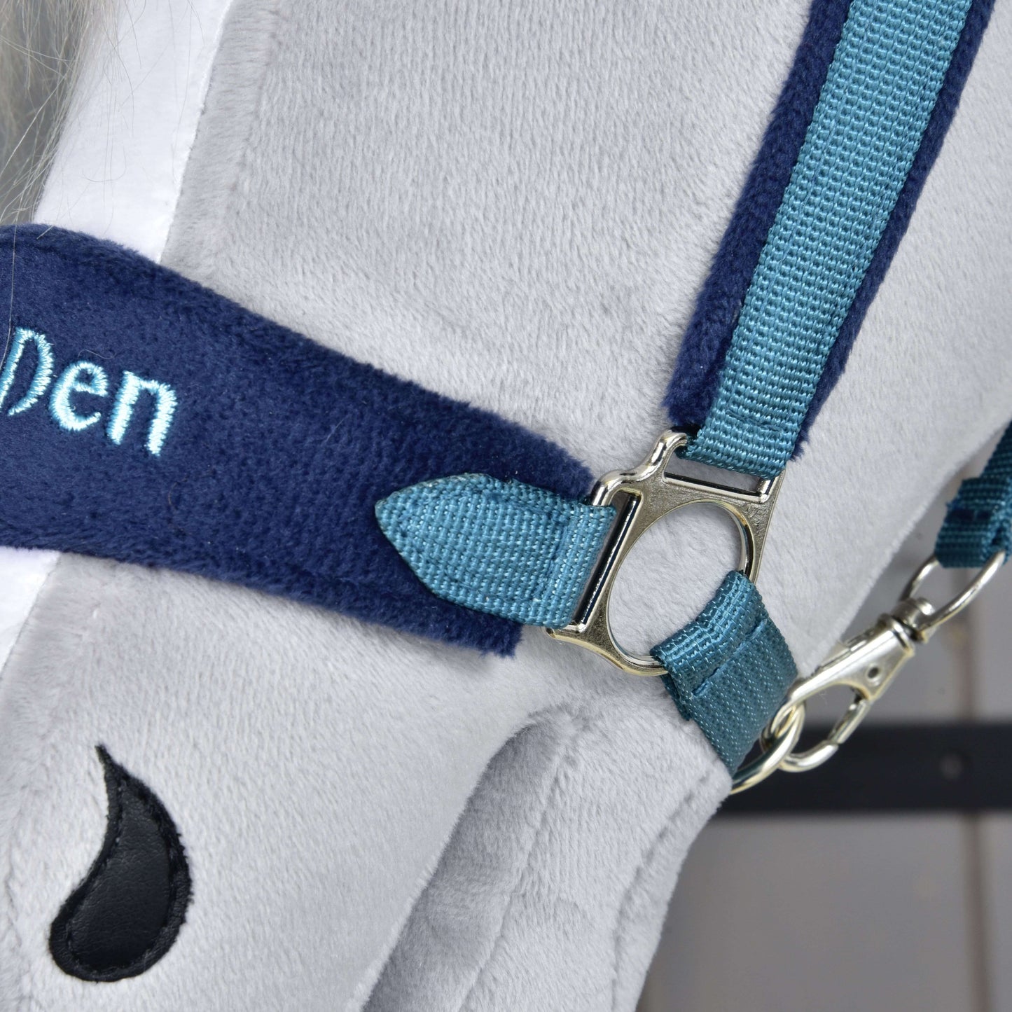 Gros plan sur le Licol en fourrure LarDen bleu de Hobby Horse LarDen, avec tissu gris doux, sangles bleues, boucle argentée, broderie « Den » partiellement visible et petit détail noir en forme de goutte. Idéal comme accessoire de licol élégant pour Hobby Horse.
