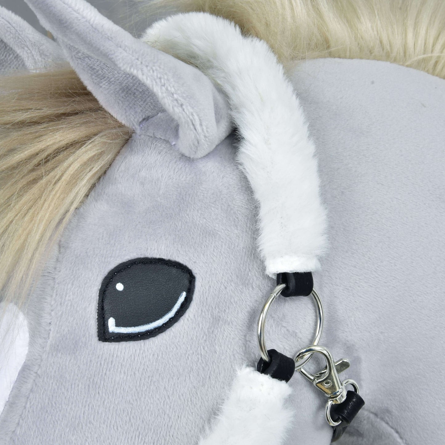 Gros plan sur le Licol en fourrure Teddy Classique de Hobby Horse LarDen : visage d’un cheval en peluche gris avec œil cousu noir et blanc, crinière blanche duveteuse, oreille douce, et licol avec anneau et fermoir argentés.