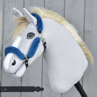 Das Hobby Horse LarDen Fellhalfter Teddy Petrol zeigt ein Plüsch-Hobby Horse mit hellgrauem Stoff, weißer Schnauze, blonder Mähne und einem blauen Halfter aus Kunstleder auf einem schwarzen Stock vor einem Holz-Hintergrund.