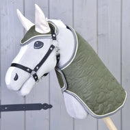 Das Set Olivetti von Hobby Horse LarDen zeigt ein graues Hobby Horse mit grüner gesteppter Decke und Zaumzeug, schwarzem Halfter für Hobby Horse, weißen Ohren und stilvollen Accessoires vor einer hellgrauen Holzwand.