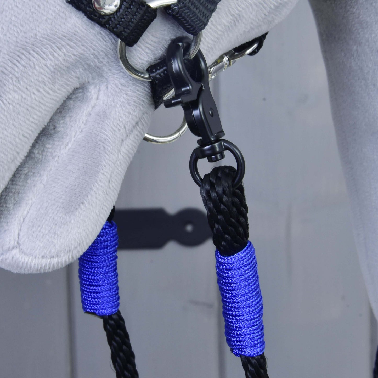 Nahaufnahme eines grauen Pferdekopfes mit schwarzem Halfter für Hobby Horse mit Hobby Horse LarDen Zügel Basic Blue – blau-schwarz geflochtene handgefertigte Zügel aus Polypropylen, befestigt an einem Metallring mit schwarzem Clip.