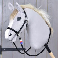 Das Plüsch-Hobby Horse von Hobby Horse LarDen hat ein hellgraues Gesicht, schwarzes Zaumzeug, eine weiße Mähne und ist auf einem Holzstab befestigt. Es wird mit handgefertigten „Zügel Emblem CZ“ geliefert, verziert mit einem blauen, weißen und roten Anhänger.