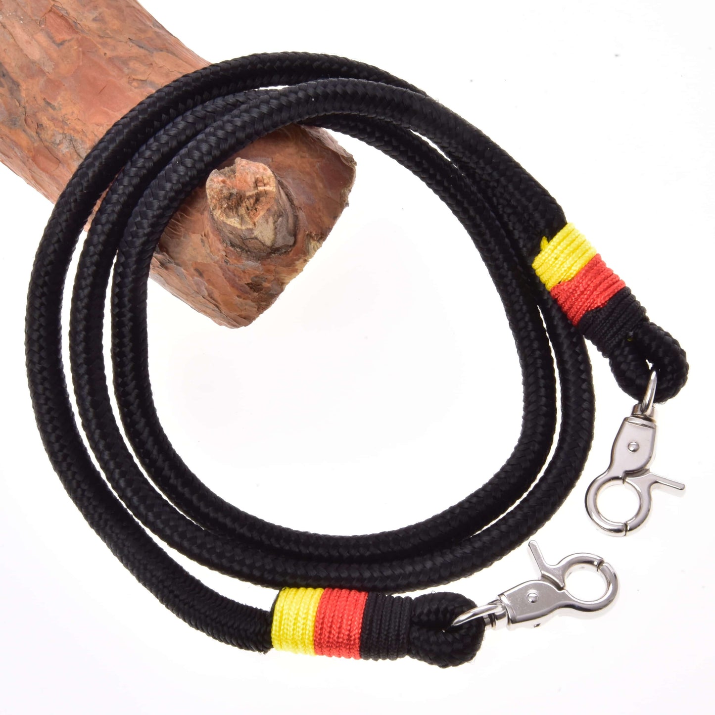The Hobby Horse LarDen Reins Emblem is a black polypropylene rope leash with metal clasps and yellow-red thread wraps, coiled on wood against a white background—ideal for handmade or hobby horse reins.