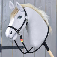 Emblème Rênes de Hobby Horse LarDen sur un Hobby Horse gris en peluche avec crinière blanche, bride noire et rênes faites main en polypropylène sur un bâton en bois, sur fond de planches de bois clair.