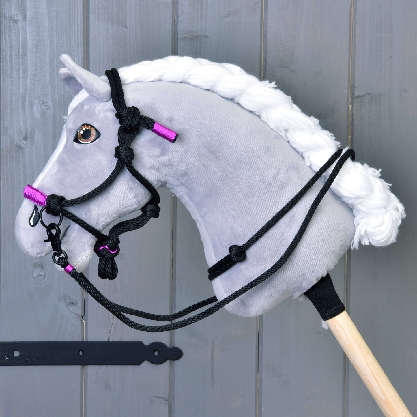 Hobby Horse LarDen Seilhalfter Violett an einem grauen Hobby Horse mit weißer Mähne, schwarzem Zaumzeug und Zügel-Details, violetten Akzenten und stilvollem Seilhalfter, montiert auf einem Holzstab vor grauer Holzwand.