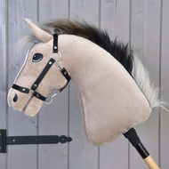 Hobby Horse Cloony mit Schwarzem Halfter von Hobby Horse LarDen, mit hellbraunem Gesicht und schwarzer Mähne, auf einem Holzstab montiert und für das Springreiten vor einer grauen Holzwand posiert.
