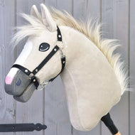 Hobby Horse Pixie mit Schwarzem Halfter von Hobby Horse LarDen mit beigefarbenem Fell, weißer Mähne, schwarzem Halfter und ausdrucksstarken Augen auf einem Stab, vor grauem Holz-Hintergrund gezeigt, in Anlehnung an den legendären metallischen Glanz der Rasse Akhal-Teke.