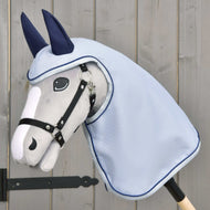 Die Hobby Horse LarDen Regendecke Luméa zeigt ein graues Plüsch-Hobby Horse auf einem Stab mit schwarzem Zaumzeug, blauer Regendecke und dunkelblauen Ohrenschützern vor hellem Holz-Hintergrund.