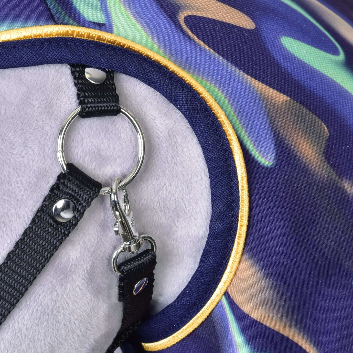 Close-up of a harness with metal rings and black straps on colorful patterned fabric with yellow trim—perfectly paired with the Raincoat rainbow by Hobby Horse LarDen for added protection over a light gray background.