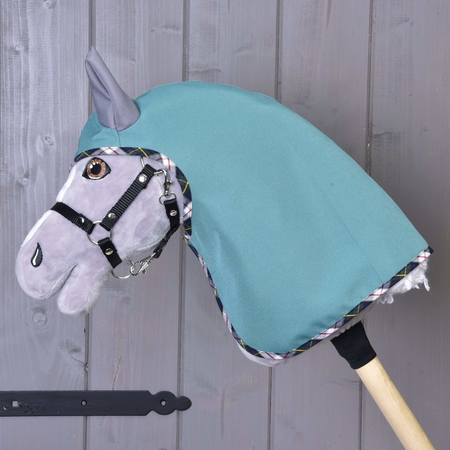 L’imperméable d'été Émeraude de Hobby Horse LarDen est présenté sur un bâton en bois, avec capuche en softshell vert émeraude et détails élégants, devant un mur en bois gris.