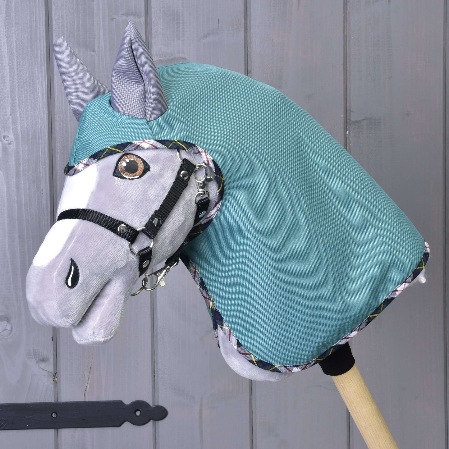L’imperméable d'été Émeraude de Hobby Horse LarDen est présenté sur un bâton en bois, avec visage gris, bride noire et couverture émeraude devant un mur en bois gris.