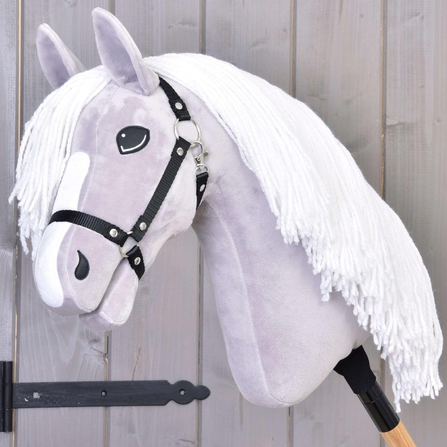 Hobby Horse LarDen Hobby Horse Popcorn mit Schwarzem Halfter mit hellgrauem Kopf, weißer Garnmähne, schwarzem Halfter und Holzstabgriff. Ideal als fantasievolles Spiel und Familien-Pferdeabenteuer. Vor einer Holzwand präsentiert.