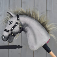 Hobby Horse Prestige mit schwarzem Halfter, Größe XS von Hobby Horse LarDen ist ein grauer Hobby Horse Kopf aus Plüsch, inspiriert von der Eleganz eines englischen Warmblut-Sportpferdes. Er hat ein ausdrucksstarkes gesticktes Gesicht, eine wilde Mähne und ein sicheres schwarzes Halfter, befestigt auf einem Holzstab. Vor hölzernem Hintergrund positioniert, ideal für fantasievolle Springabenteuer.