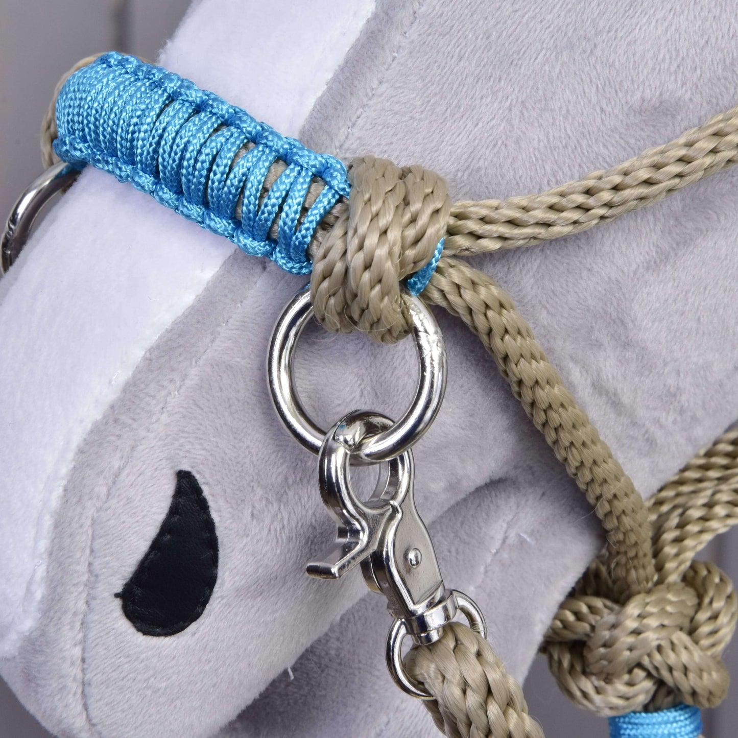 Nahaufnahme eines grauen Plüschkopfes von Hobby Horse LarDen mit dem Seilset Nature Blue, mit blau-beigem Halfter für Hobby Horse mit Metallring und Clip, schwarzem gesticktem Auge, weißer Schnauze und passend befestigten Zügeln.