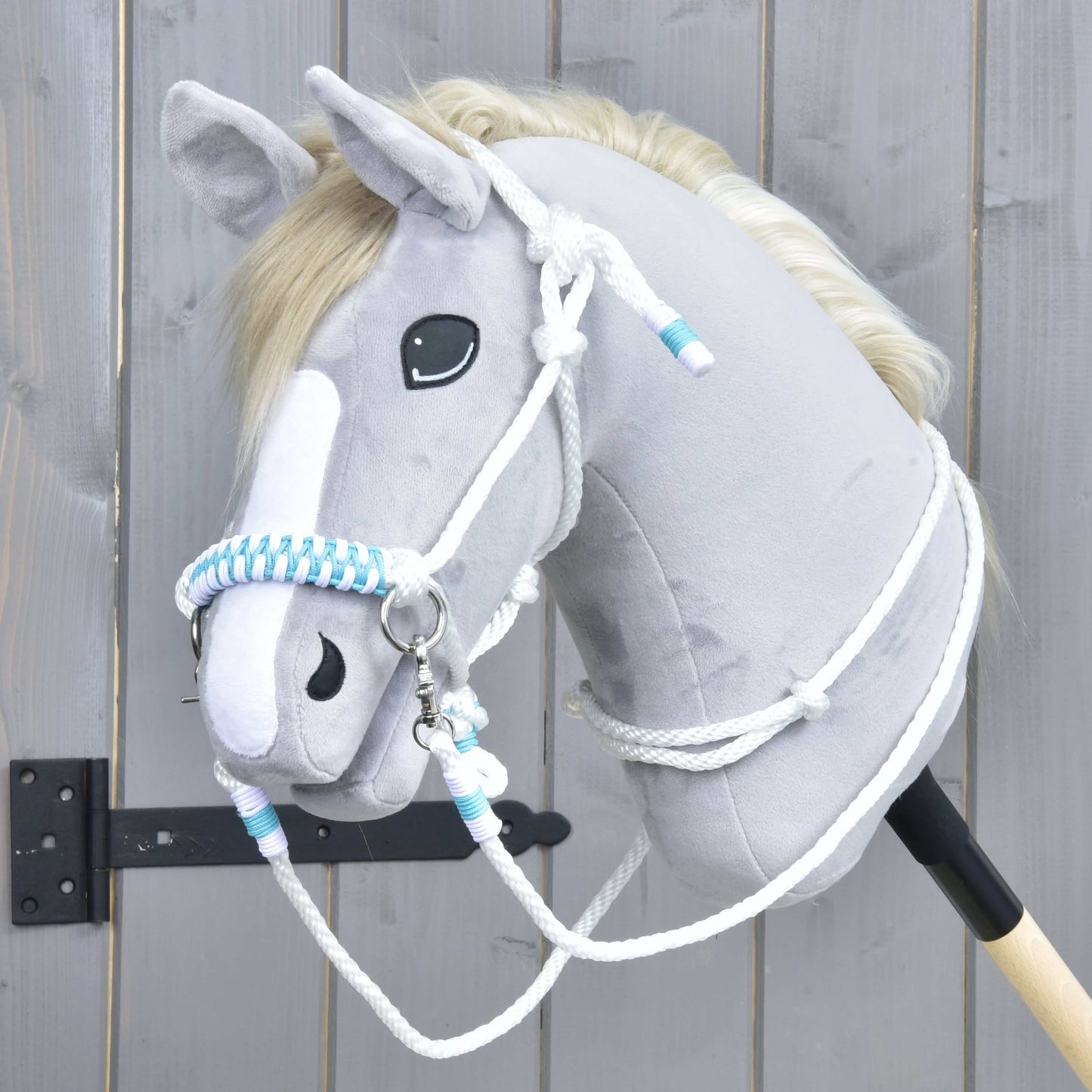 Ensemble de corde Reine Blanche de Hobby Horse LarDen avec tête de Hobby Horse en peluche à fourrure gris clair, crinière blanche et liste blanche, rênes tressées bleues et blanches, présenté devant une clôture en bois.