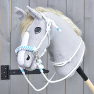 Seilset White Queen von Hobby Horse LarDen mit plüschigem Hobby Horse-Kopf mit hellgrauem Fell, weißer Mähne und weißem Gesichtsstreifen sowie blau-weiß geflochtenen Zügeln, gezeigt vor einem Holzzaun.