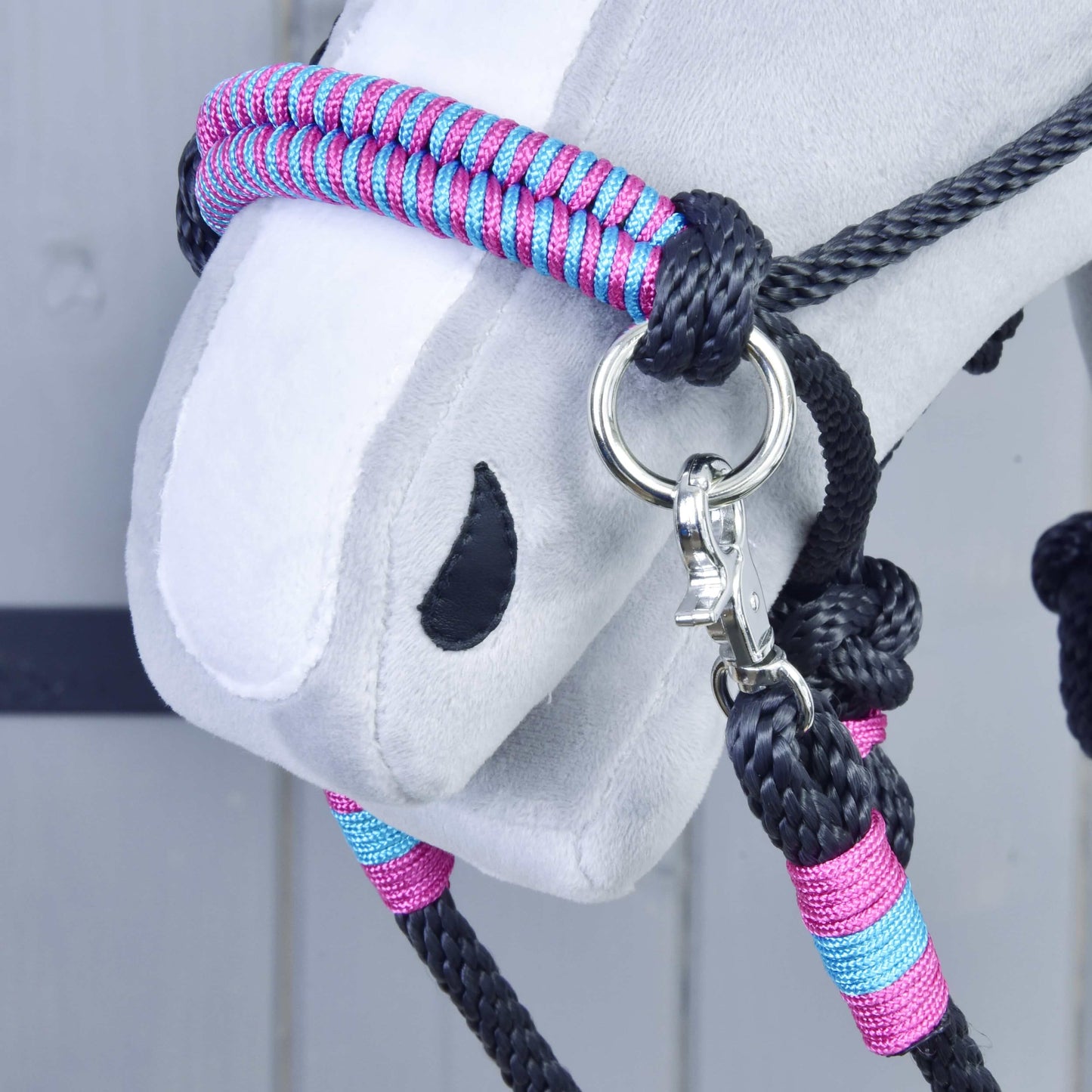 Close-up of a Hobby Horse LarDen Rope set Princess on a plush hobby horse’s head—a black, pink, and blue braided halter with metal rings and clip—perfect for imaginative riding setups against a light grey wooden backdrop.
