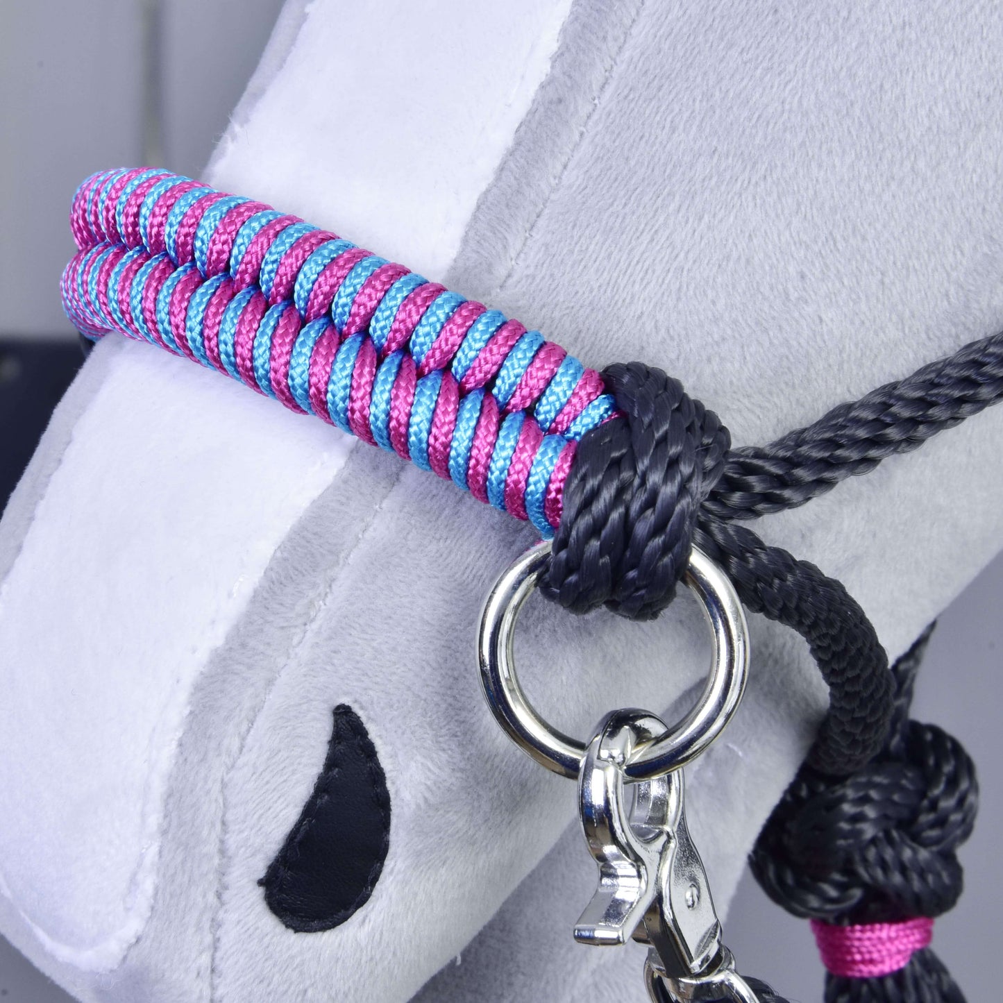 Close-up of a gray plush hobby horse's head, featuring the "Rope set Princess" by Hobby Horse LarDen—a pink and blue braided halter with black rope details, metal ring, and silver clip. Black stitching forms nostrils and eyes for imaginative play.