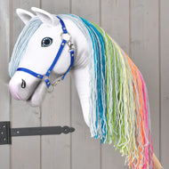 Hobby Horse Rainbow New de Hobby Horse LarDen avec corps blanc, longue crinière arc-en-ciel en fil et licol bleu pour un style féerique, sur un revêtement en bois gris avec une charnière en métal noir à gauche