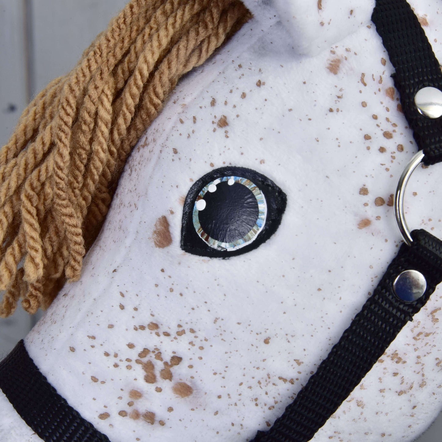 Gros plan de « Rufus avec licol noir » de Hobby Horse LarDen : un Hobby Horse Appaloosa blanc avec crinière brune en fil, licol noir, œil cousu noir et blanc, et tissu en peluche avec taches brunes comme un étalon Appaloosa.