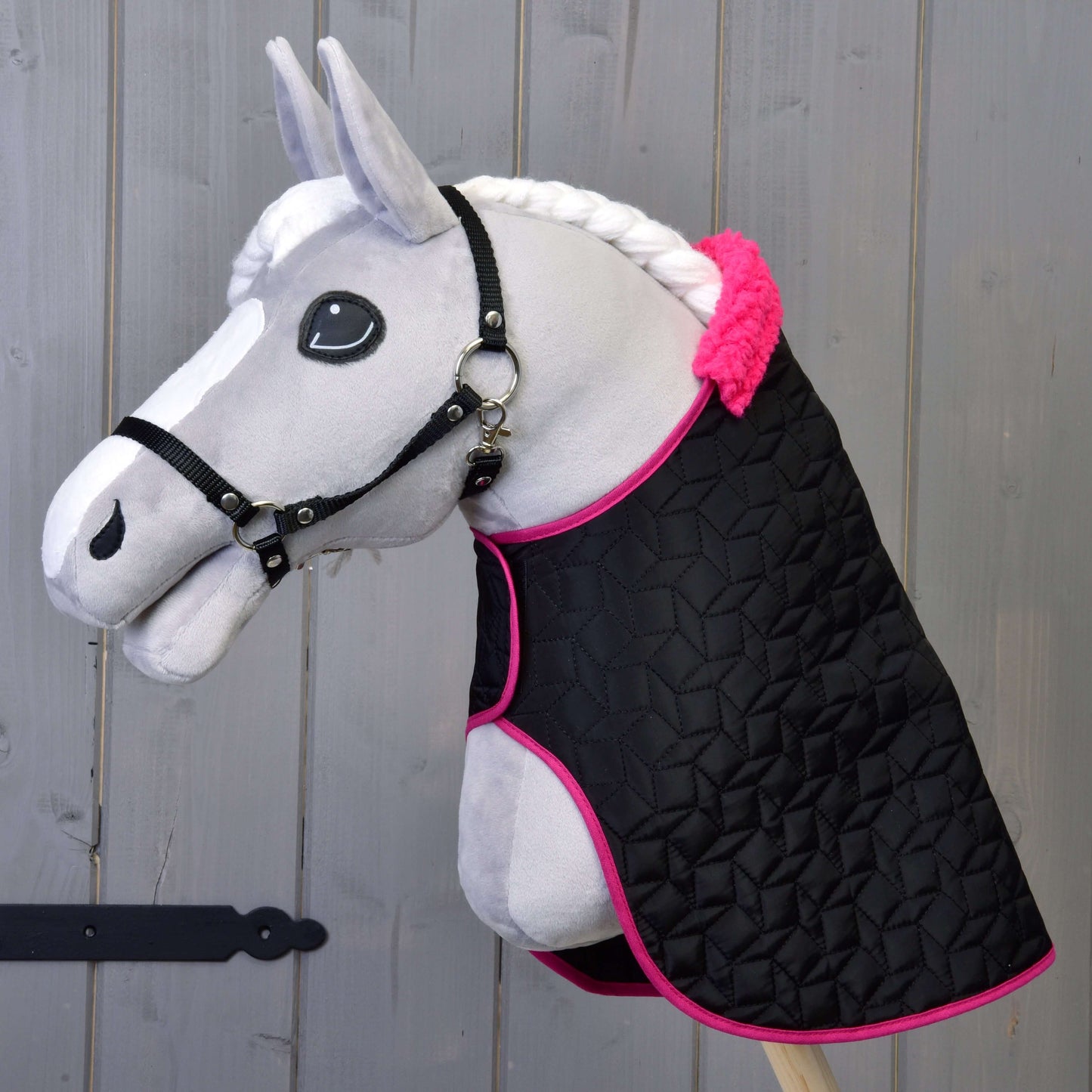 Hobby Horse blanc de Hobby Horse LarDen avec rênes noires et Ensemble Thermo Noir avec Fourrure devant un fond en bois, mettant en valeur une crinière tressée, un œil expressif de style cartoon et un bonnet d'oreilles élégant.