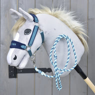 Set LarDen Exclusive Blue von Hobby Horse LarDen, ein weiches Hobby Horse am Stock mit hellgrauem Gesicht, blauem Halfter für Hobby Horse mit Fleece-Nasenriemen und geflochtenem Führstrick, vor Holz-Hintergrund.