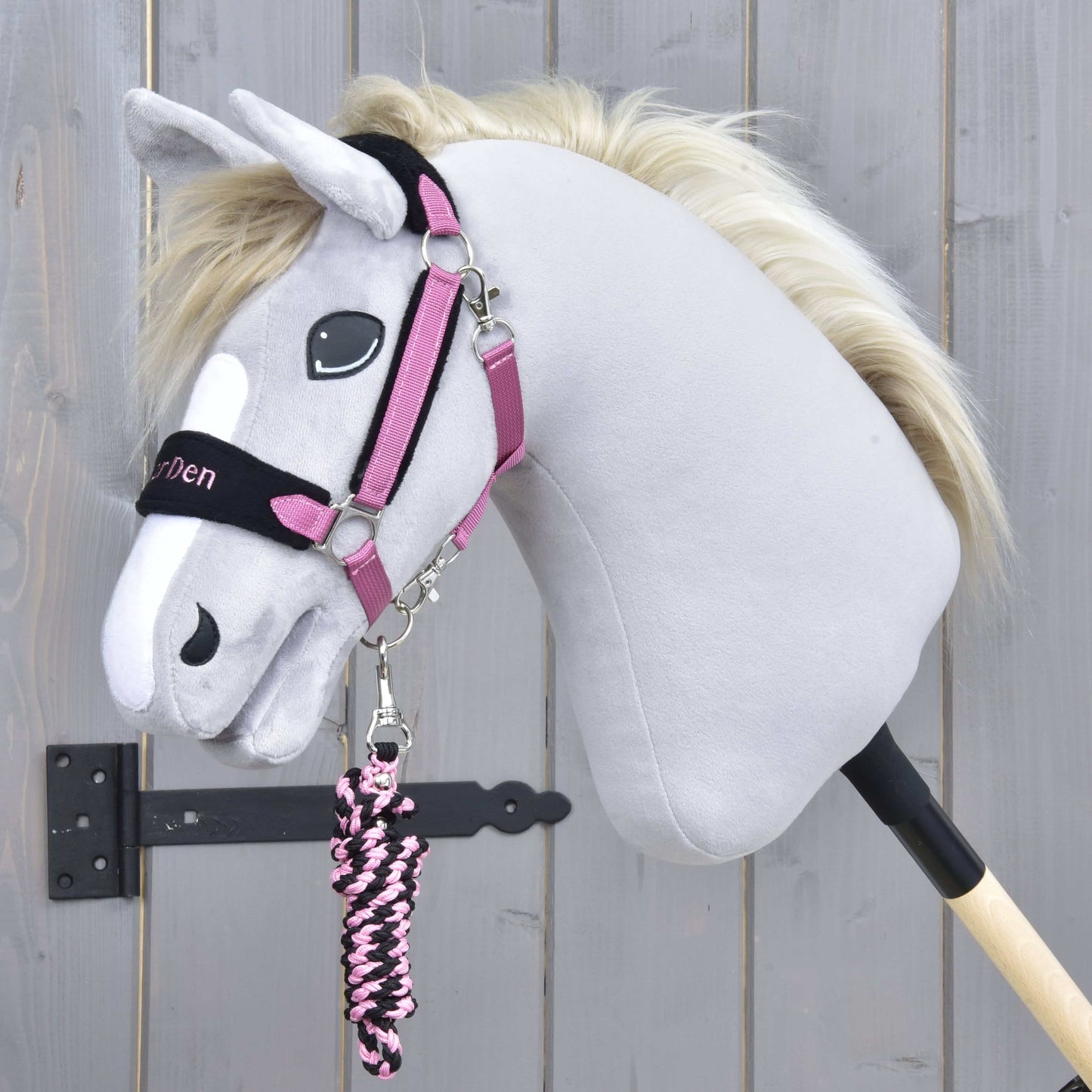 Set LarDen Exclusive Pink von Hobby Horse LarDen mit grauem Hobby Horse mit weißer Blesse, flauschiger Mähne, comicartigen Augen, Halfter für Hobby Horse in Schwarz und Pink mit Fleece-Nasenriemen sowie passendem pink-schwarzem Führstrick an einem Stock.