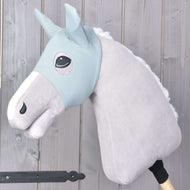 Masque Hobby Horse Spiky de Hobby Horse LarDen sur un cheval en peluche gris avec bride bleu clair, crinière blanche et masque de protection sur un bâton en bois, présenté sur un fond de planches en bois clair.
