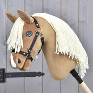 Hobby Horse LarDen „Hobby Horse Smart mit Schwarzem Halfter“ mit plüschigem hellbraunem Gesicht, weißer Garnmähne und schwarzem Halfter an einem Holzstab, präsentiert vor einer grauen Holzwand.