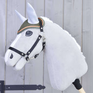 Ein plüschiges Hobby Horse von Hobby Horse LarDen auf einem Stab mit weißer Mähne, grauem Gesicht, schwarzem Zaumzeug und gesticktem Auge trägt die Ohrenkappe Sport – eine grüne Ohrenkappe mit orangefarbener Einfassung – vor hellem Holz-Hintergrund.