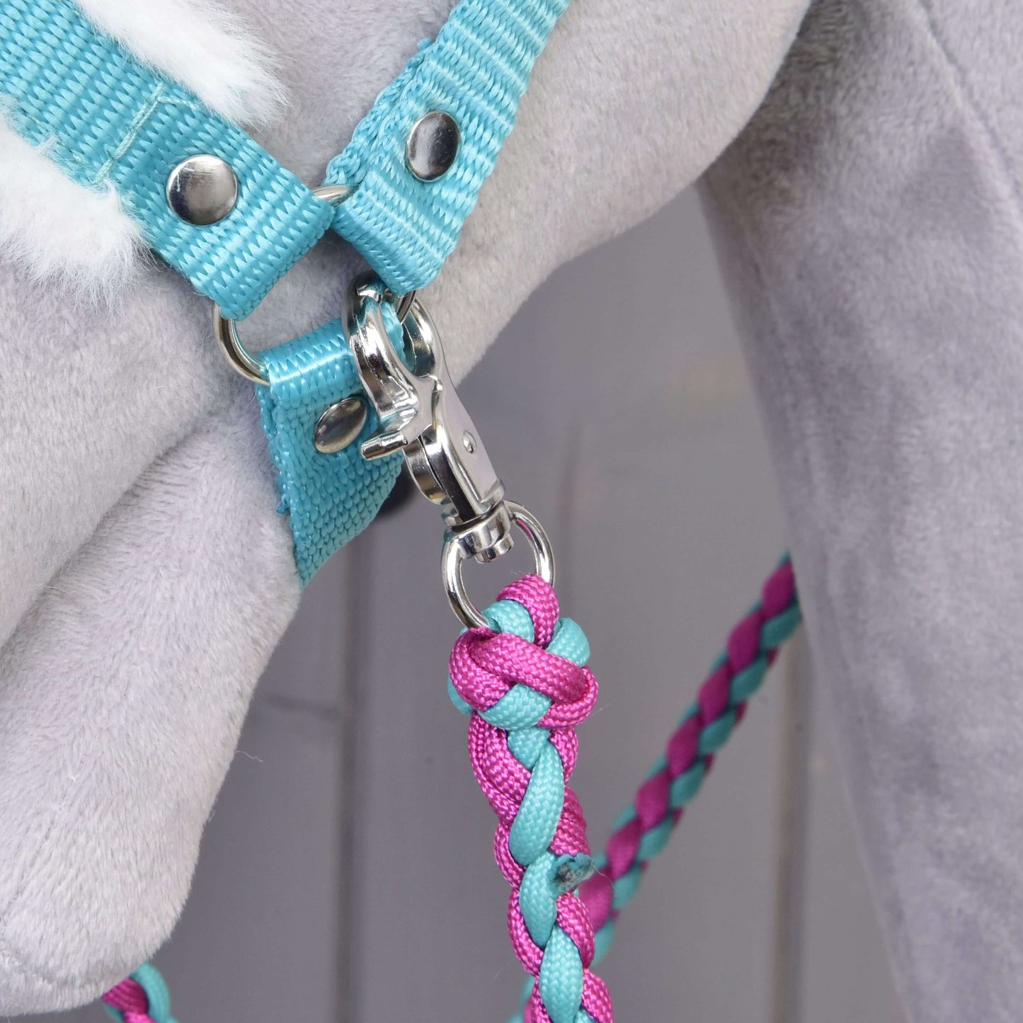 Gros plan sur l’Ensemble Combinaison Parfaite Turquoise de Hobby Horse LarDen, avec une longe tressée rose et bleue attachée à un licol turquoise rembourré de fourrure sur un Hobby Horse en peluche gris clair, idéal pour les amateurs d’accessoires pour Hobby Horse.