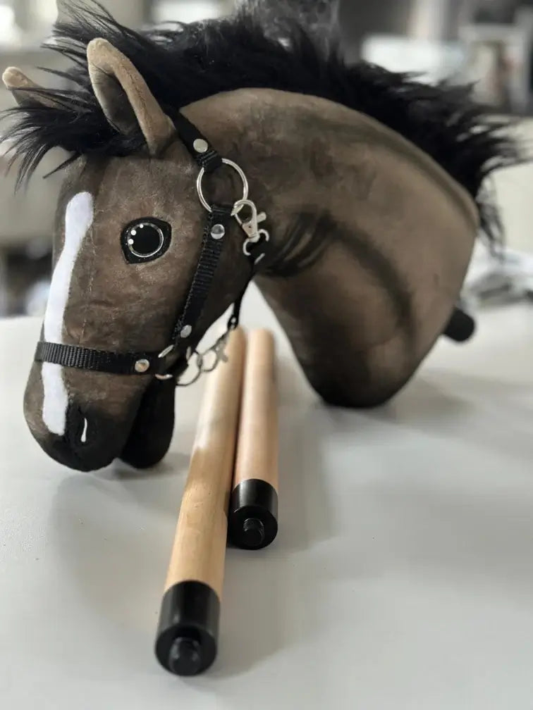 Ein Plüsch-Hobby Horse-Kopf mit schwarzer Mähne und Halfter liegt auf einem Tisch neben zwei Holzstäben mit schwarzen Kappen, perfekt für Begeisterte des Hobby Horsing.