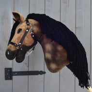 Hobby Horse Stormy mit Schwarzem Halfter von Hobby Horse LarDen aus braunem Plüsch mit schwarzer Garnmähne, auf einer Metallhalterung vor einer Holzwand.