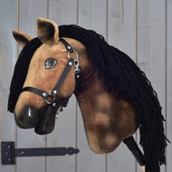 Hobby Horse Stormy mit Schwarzem Halfter von Hobby Horse LarDen mit braunem Plüsch im Hannoveraner-Design, schwarzer Garnmähne, schwarzem Halfter und weißen Abzeichen, auf einem Stab vor grauem Holzhintergrund.