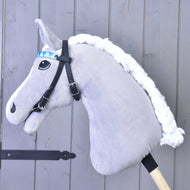 The Hobby Horse LarDen Bridle with 2 headbands turquoise (Size M), on a gray plush hobby horse with a white mane and wooden stick, is shown against a light gray wooden wall.