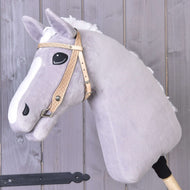 Die Hobby Horse LarDen Westerntrense Classic, ein hellgraues Plüsch-Hobby Horse mit weißer Blesse und schwarzen Augen an einem Holzstab, verfügt über eine stilvolle Westerntrense und ist vor einem Hintergrund aus grauen Holzplanken dargestellt.
