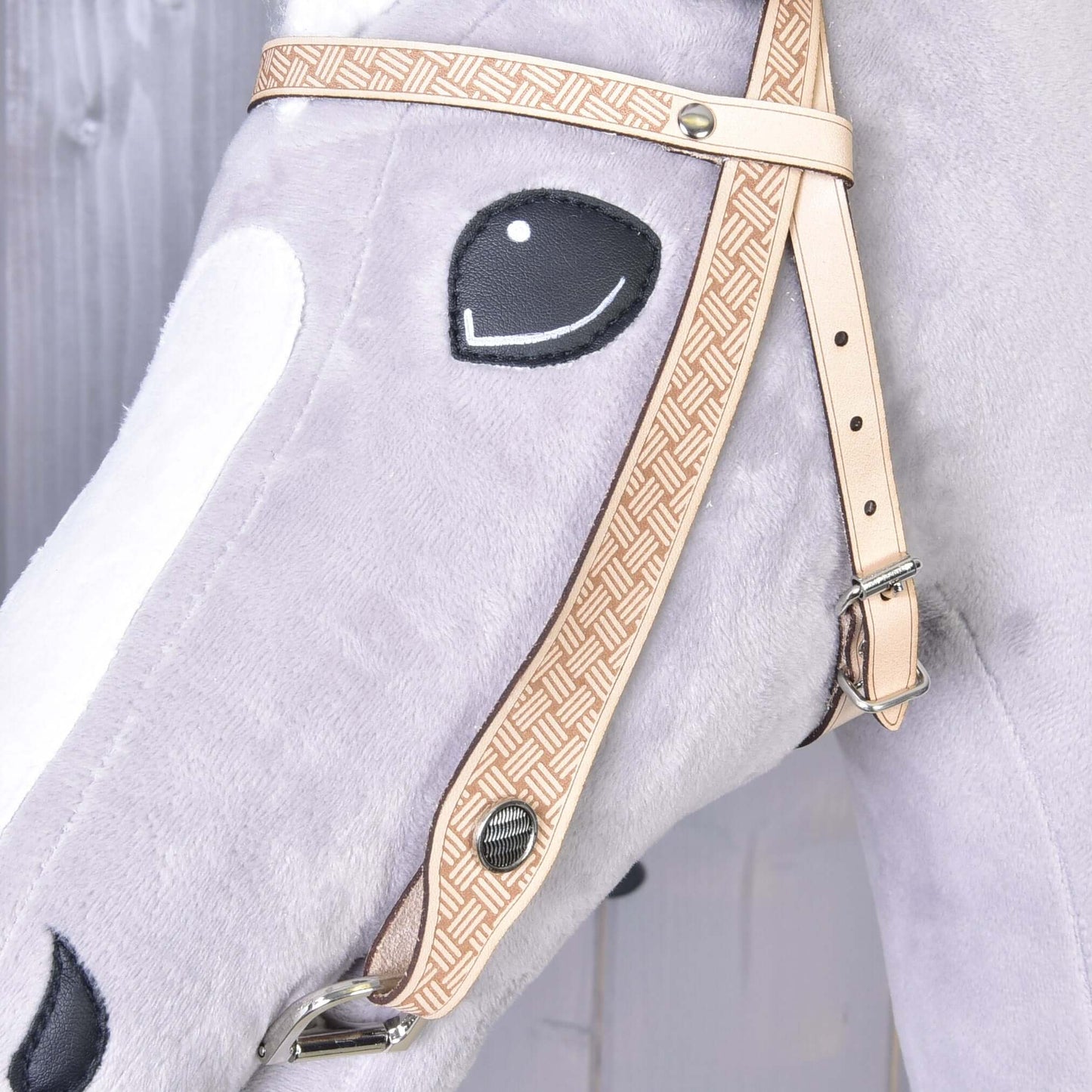 Gros plan sur la Bride Western Classique de Hobby Horse LarDen : élégante tête de cheval en peluche gris clair avec bride beige à motif et œil noir brodé, sur un fond en bois clair.