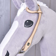 Nahaufnahme eines Plüschpferdekopfes aus hellgrauem und weißem Stoff mit aufgesticktem schwarzem Auge und Westerntrense Einohr von Hobby Horse LarDen mit silberfarbenen Beschlägen vor Holz-Hintergrund.