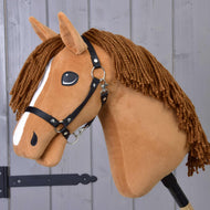 Hobby Horse LarDen „Hobby Horse Wendy mit Schwarzem Halfter“ ist ein Plüschtier in Form einer Fuchsstute mit brauner Garnmähne, weißem Gesichtsstreifen und schwarzem Halfter für Hobby Horse – ideal als fantasievolles Spielzeug – vor einem Hintergrund aus Holzpaneelen.