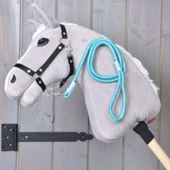 Hobby Horse - Führstrick Atlantis von Hobby Horse LarDen mit grauem Plüschkopf, schwarzem Zaumzeug für Hobby Horse, blauem Führstrick und Holzstab vor senkrechten Holzplanken