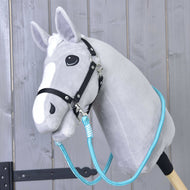 Rênes Atlantis de Hobby Horse LarDen sur un Hobby Horse gris en peluche avec bride noire et rênes bleues en corde de polypropylène, monté sur un bâton en bois devant un mur rustique en bois.