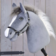 Hobby Horse Beauty mit Schwarzem Halfter von Hobby Horse LarDen mit grauem Plüschhengstkopf, weißer Mähne und Holzstock, vor einem Holzzaunhintergrund.