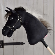 Hobby Horse Bond mit Schwarzem Halfter von Hobby Horse LarDen, ein schwarzes Hobby Horse aus Plüsch mit weißer Mähne, schwarzem Halfter und Zügeln an einem Holzstock, vor einer hellen Holzwand – perfekt für jeden Hobby Horse Bond-Fan.